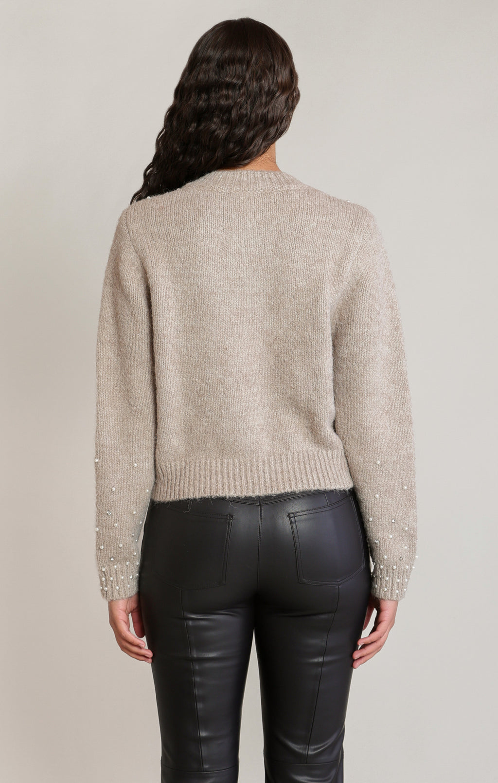 Beige Dex knit cardigan with pearl and crystal buttons, embellishments across the upper front and lower sleeves, and ribbed trim, styled with black pants